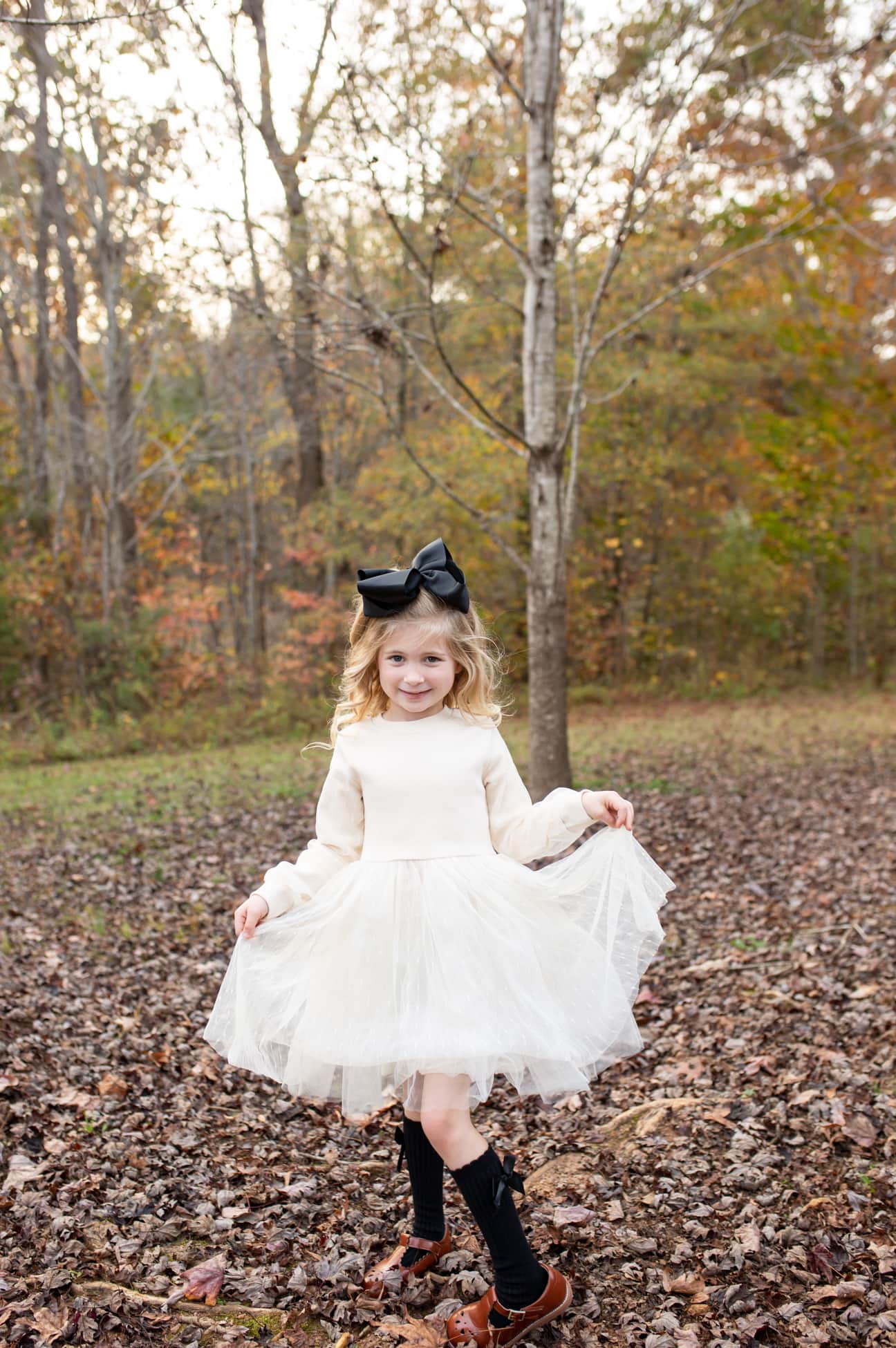 cute girls showing off her white dress and black bow during a fall photo session in a park in Wake Forest, NC