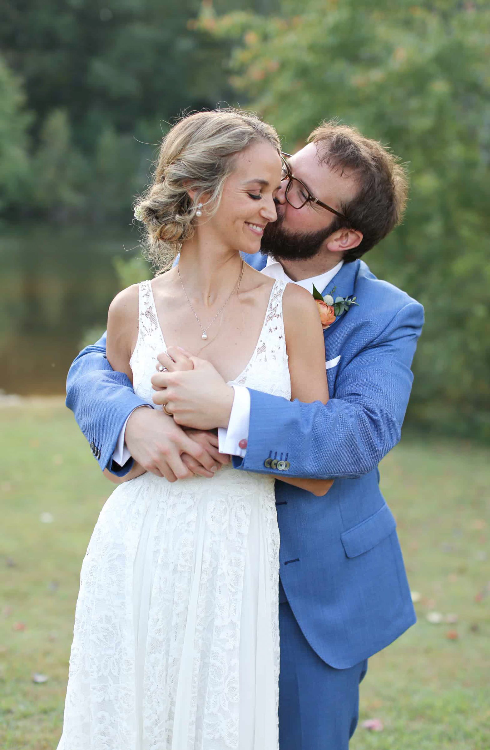 groom in a blue suit kissing his bride wearing white during romantic photo session in chapel hill north carolina