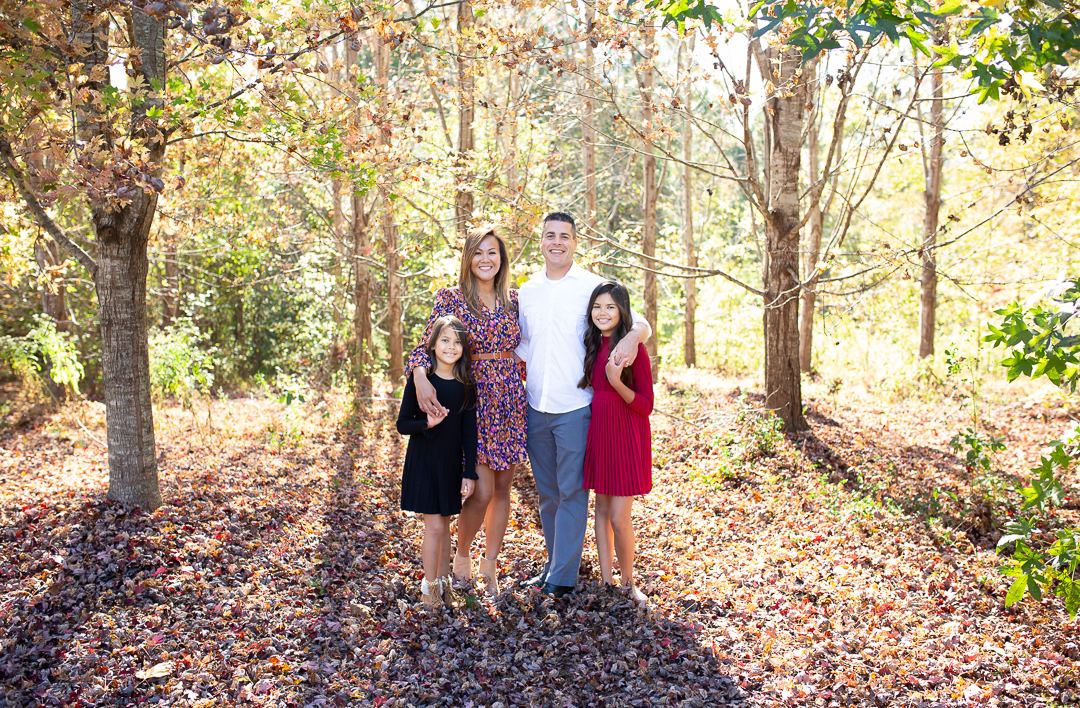 mini sessions in Wake Forest, NC. A family of four smiling at the camera in a fall forest.