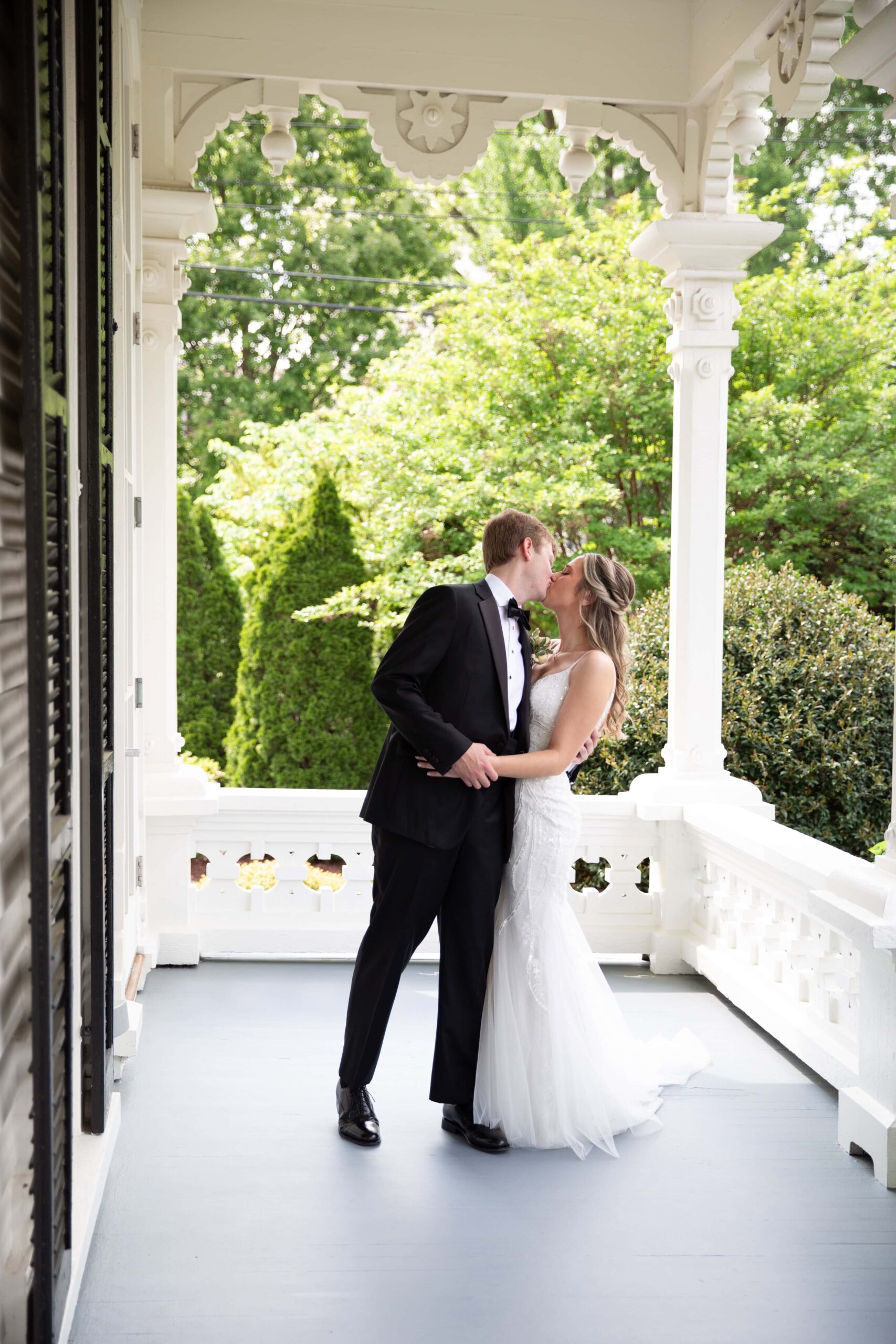 newlyweds kissing on a porch of Merrimon-Wynne House captured by Raleigh NC wedding photographer