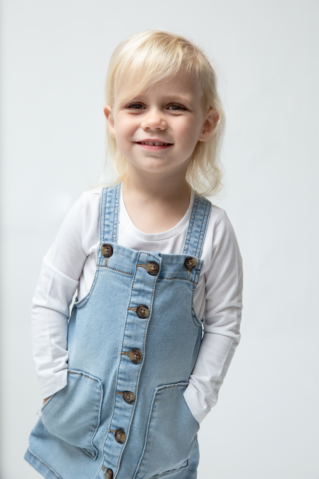 cute toddler girl smiling at the camera and wearing jean dress