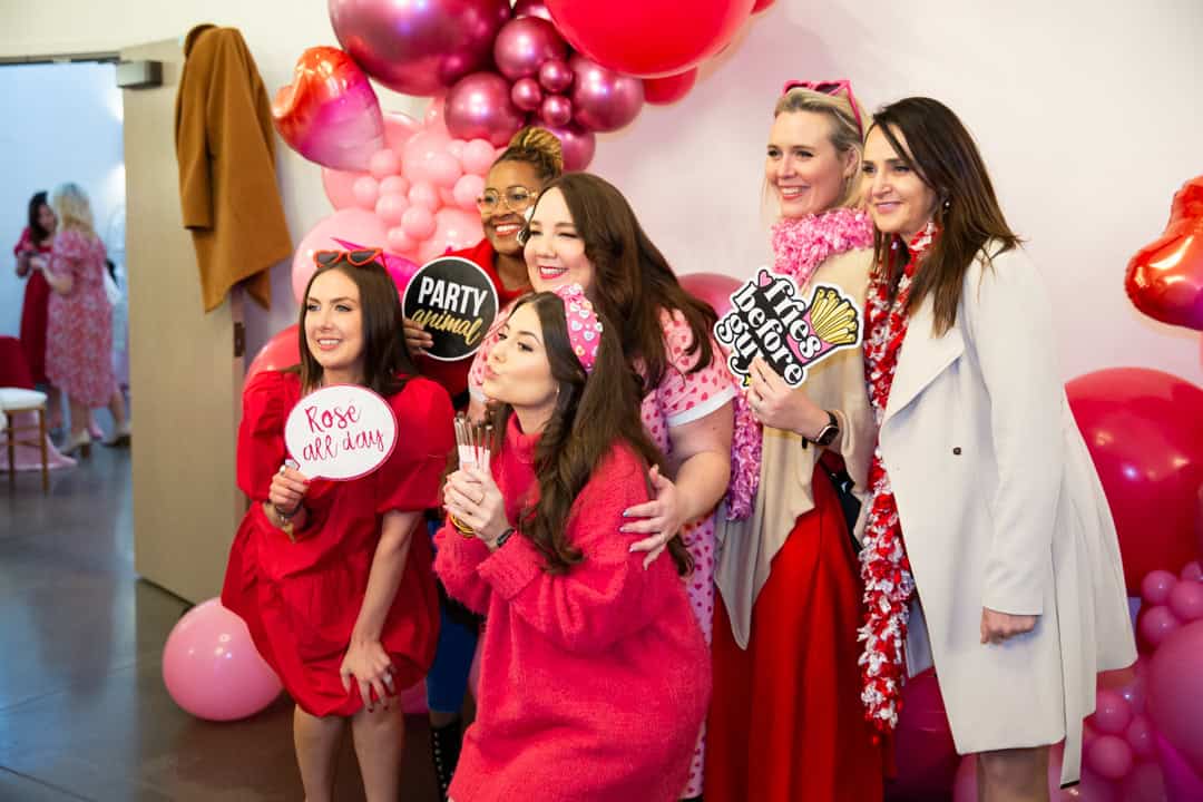 Galentine's day themed party at the Maxwell Raleigh, NC. Ladies wearing reds and pink outfits posing at a photobooth.