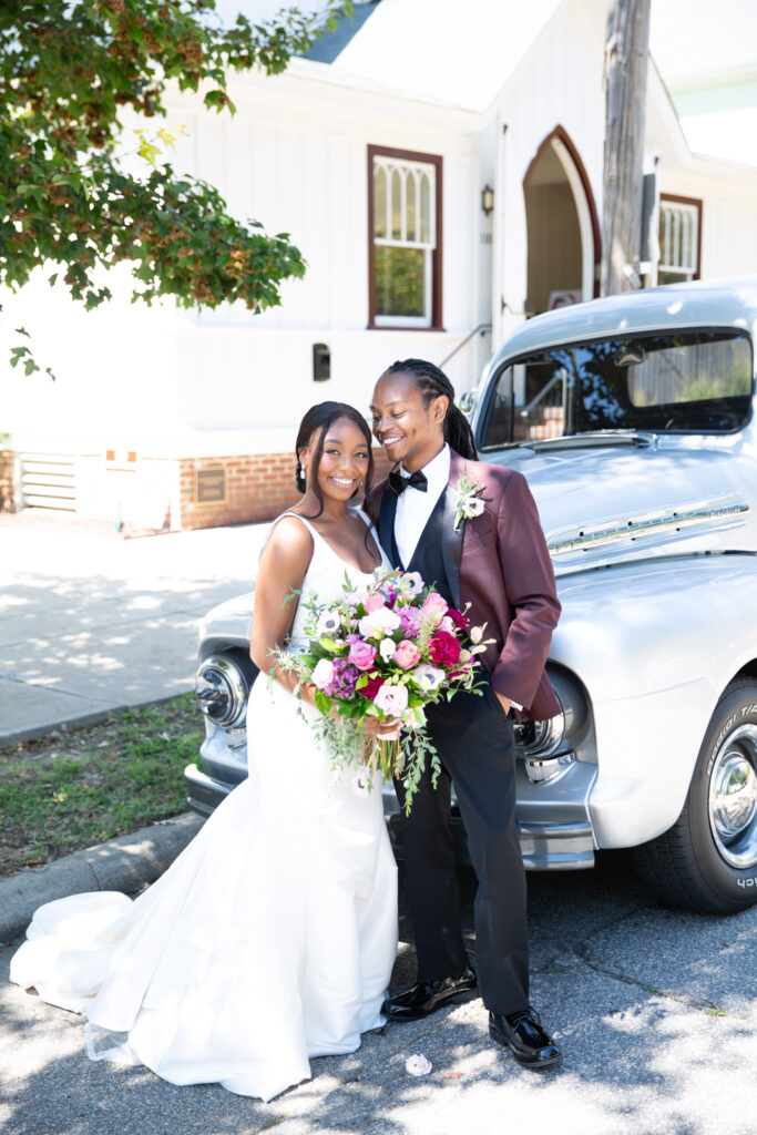 Newlyweds standing by a vintage car in front of All Saints Chapel in Raleigh. All Saints Chapel Raleigh wedding photographer.