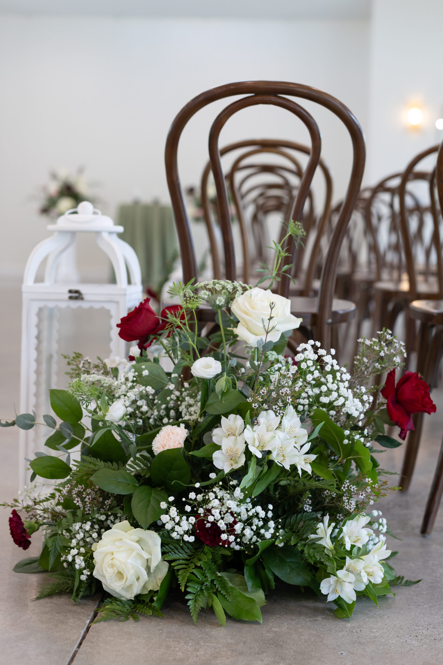 White and deep red roses, baby's breath. carnations and lush dark greenery floral arrangement for the aisle. 