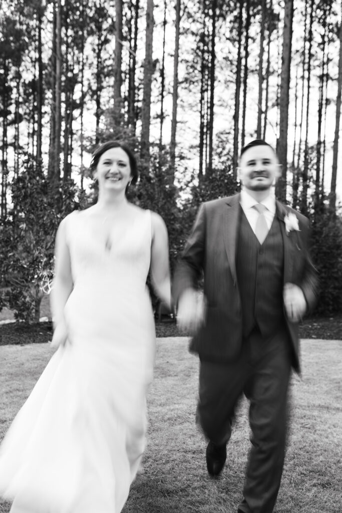 Black and white motion blurred capture of Bride and Groom running towards the camera smiling. Magdalena Stefanek Photography, Raleigh wedding photographer.