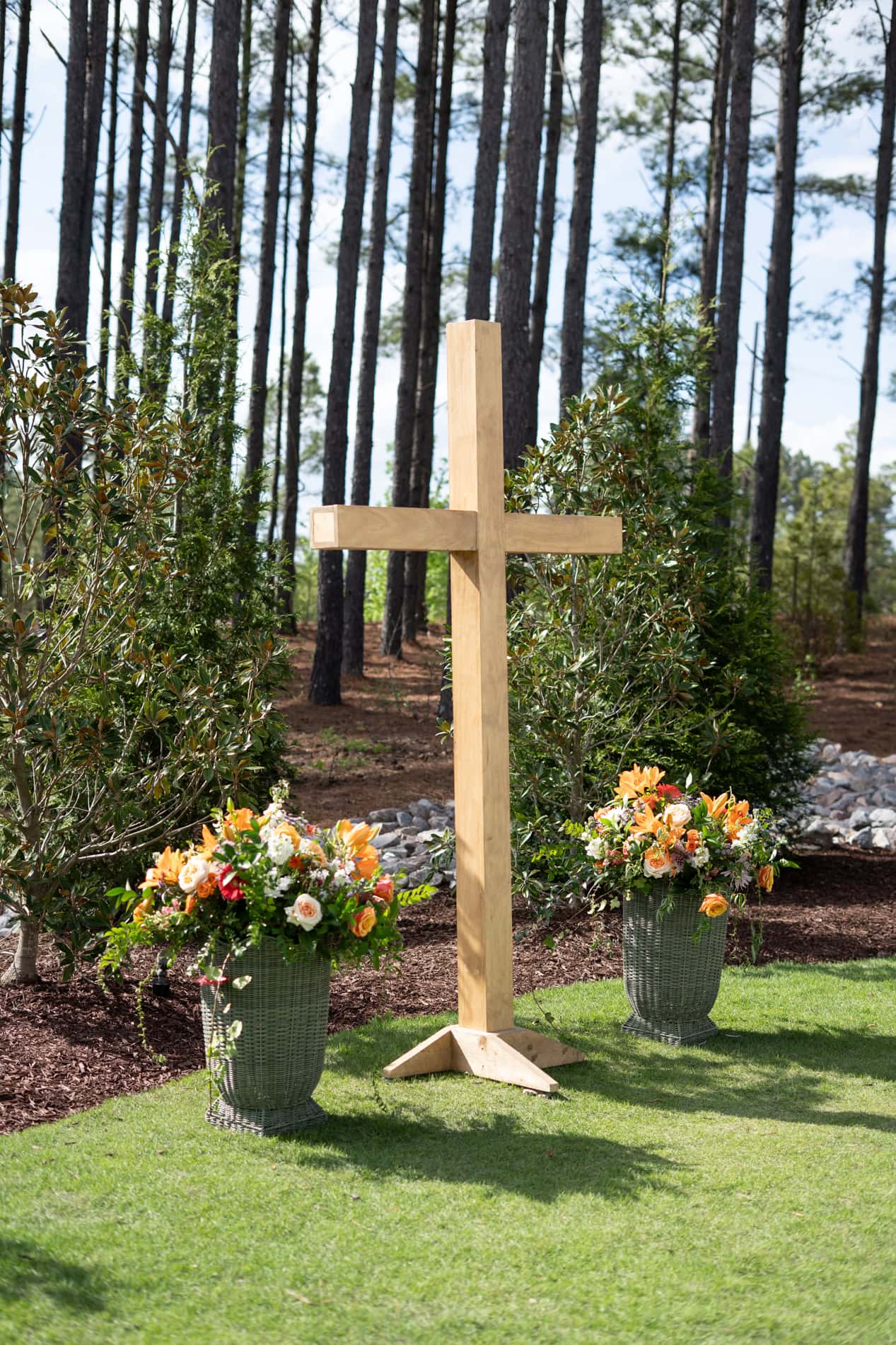 wooden cross and colorful spring florals with pine trees in the background.