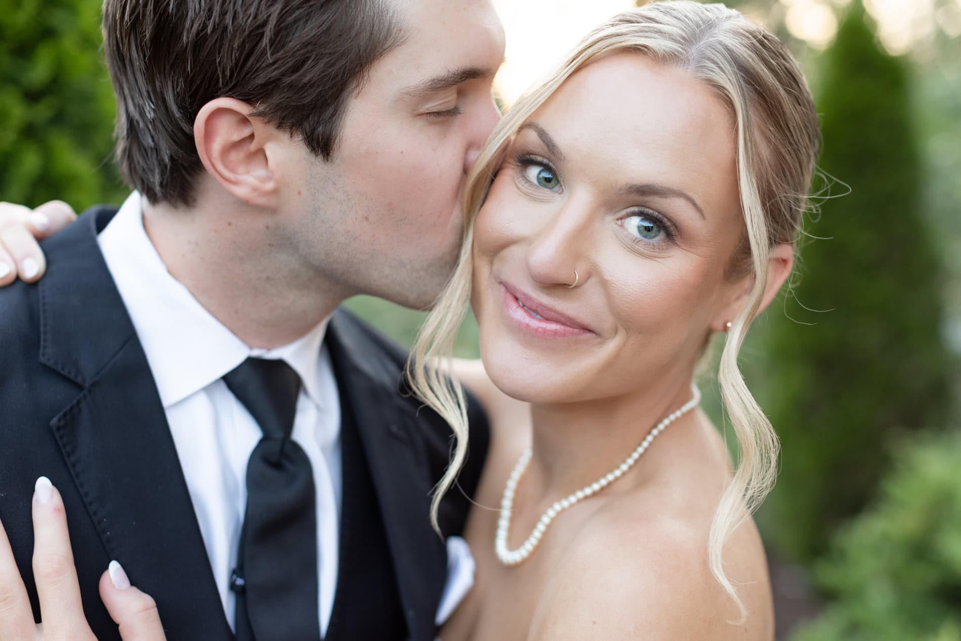 Groom kissing brides cheek while she looks at the camera and smiles. Sunset photo at the Upchurch Cary by The Upchurch Wedding Photographer.