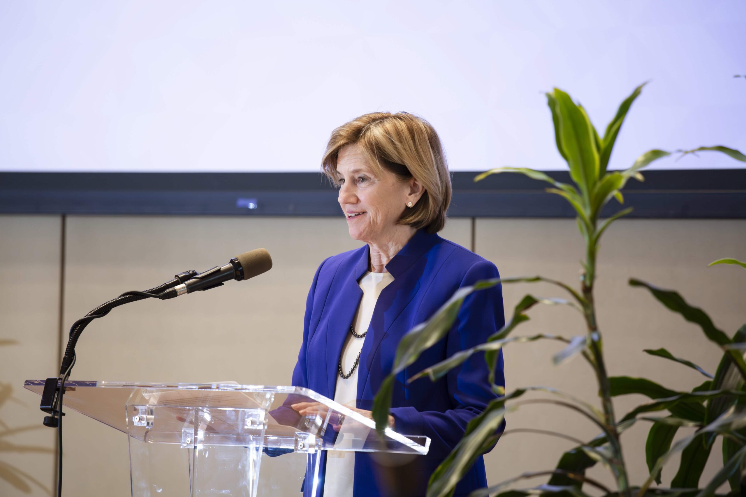 corporate photo of a woman speaking in front of microphone. 